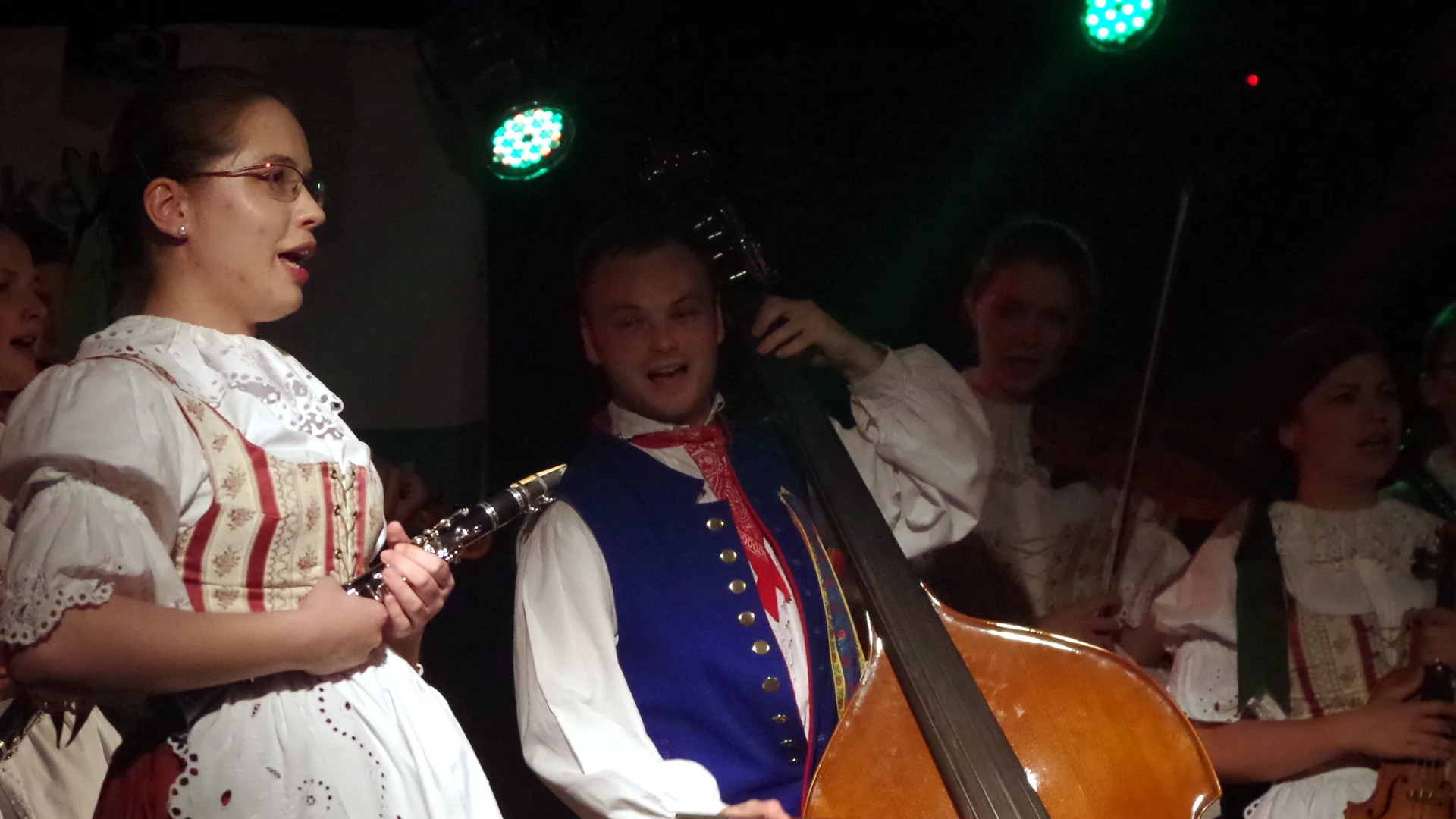 Česká lidová kapela v krojích hraje večer na pódiu — klarinet, zpěvák a kontrabas, ilustrační snímek k českému folklornímu večeru