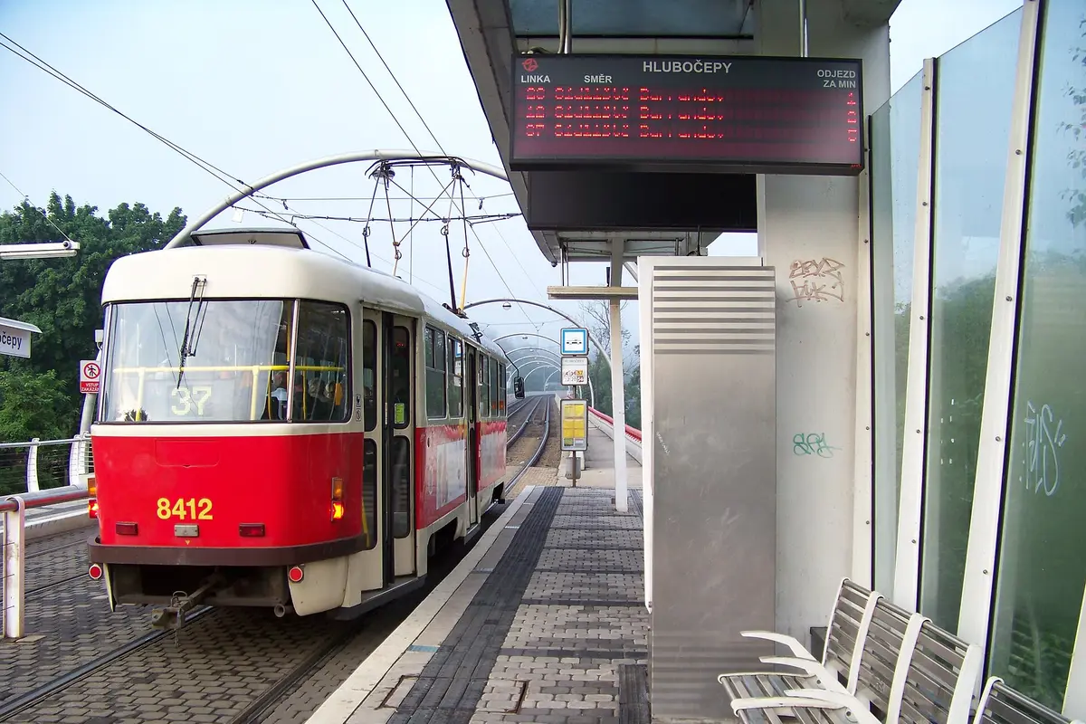 A red tram waiting at the covered Hlubočepy stop beside a departures board